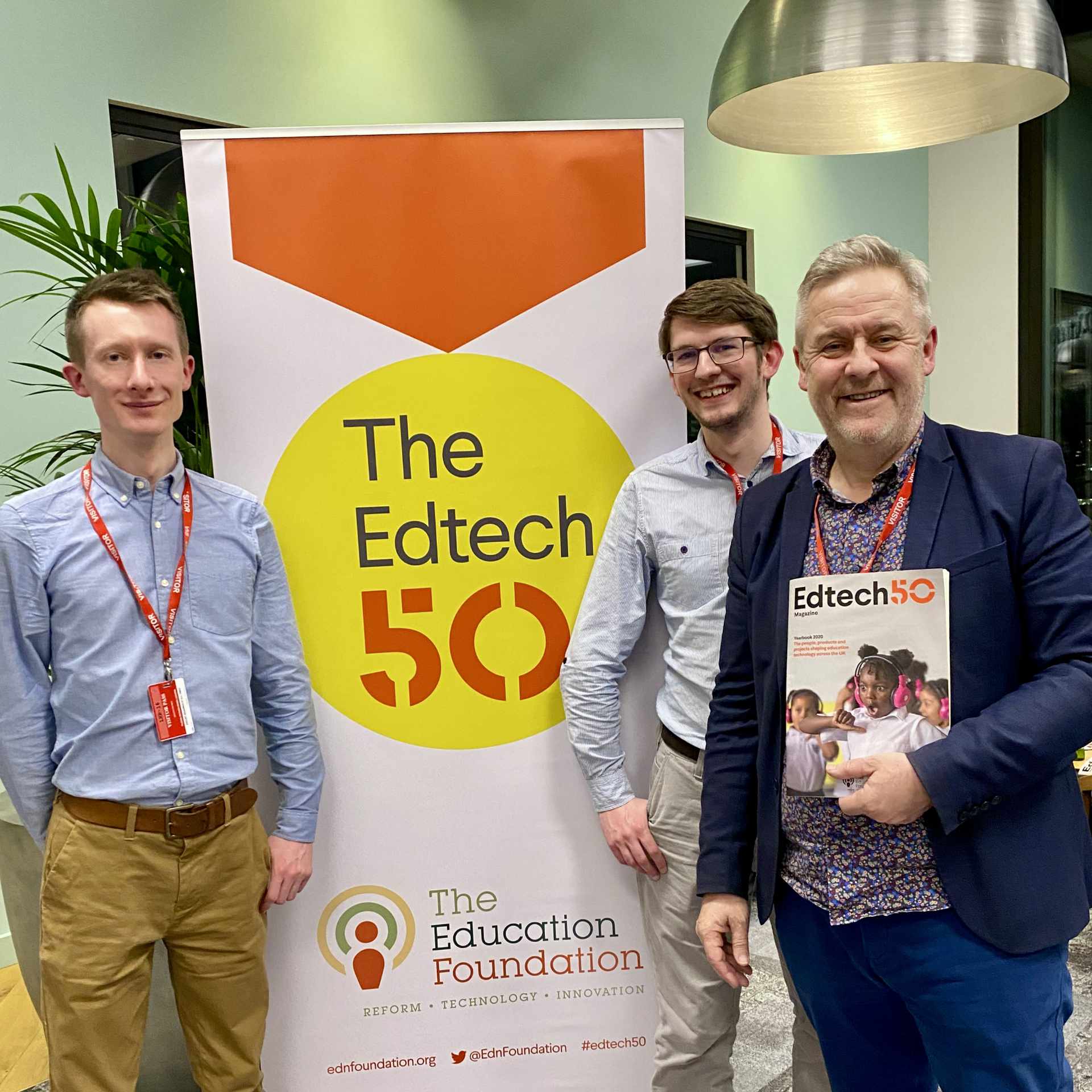 Three people stand in front of an 'Edtech50' banner; one holds an Edtech yearbook.